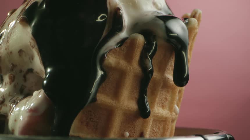 Chocolate sauce is dripped on top of ice cream in a waffle cone in a bowl during a photo shoot