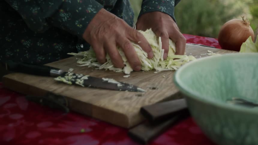 A man outside puts chopped lettuce in to a bowl