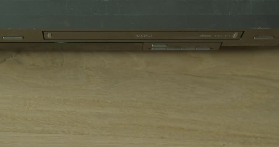 A person presses the eject button on a video cassette player and removes the tape