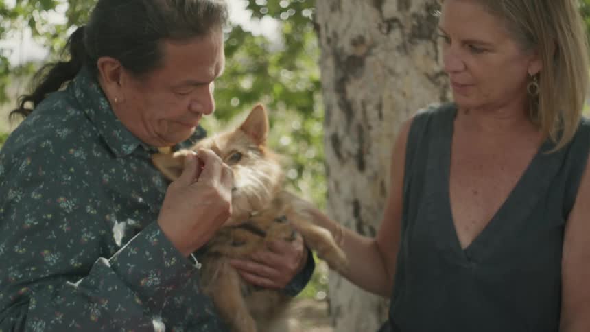 A couple pets their dog as they sit at a table covered in food