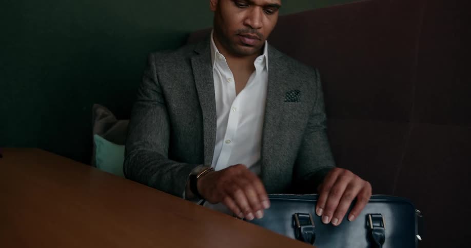 Professional black man sitting at the desk putting his laptop in his suitcase