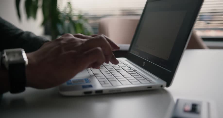 Professional man sitting at the desk in an office space typing on his laptop