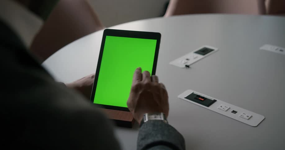 Man with gray blazer jakcet and wristwatch sits at table using tablet