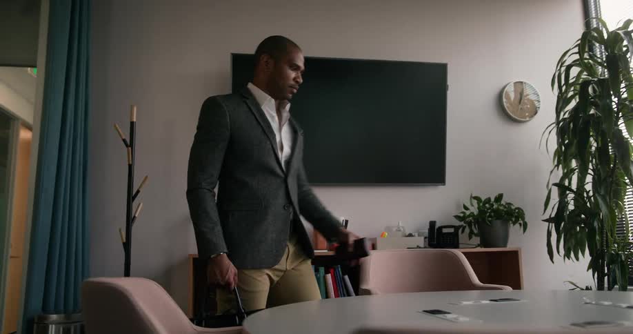 A man enters an office with a round conference table and takes out his laptop