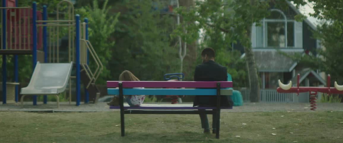 A man is sitting on a park bench and a little girl is sitting at the other end of the bench holding her knees