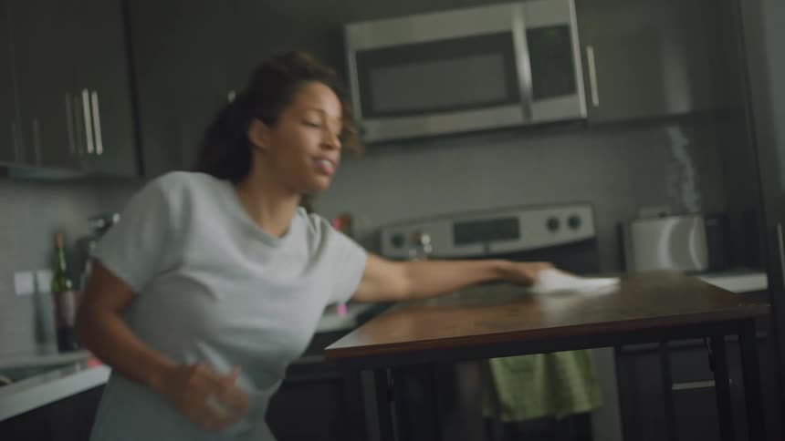 A woman dances while using a paper towel to clean a table in a home kitchen during the day