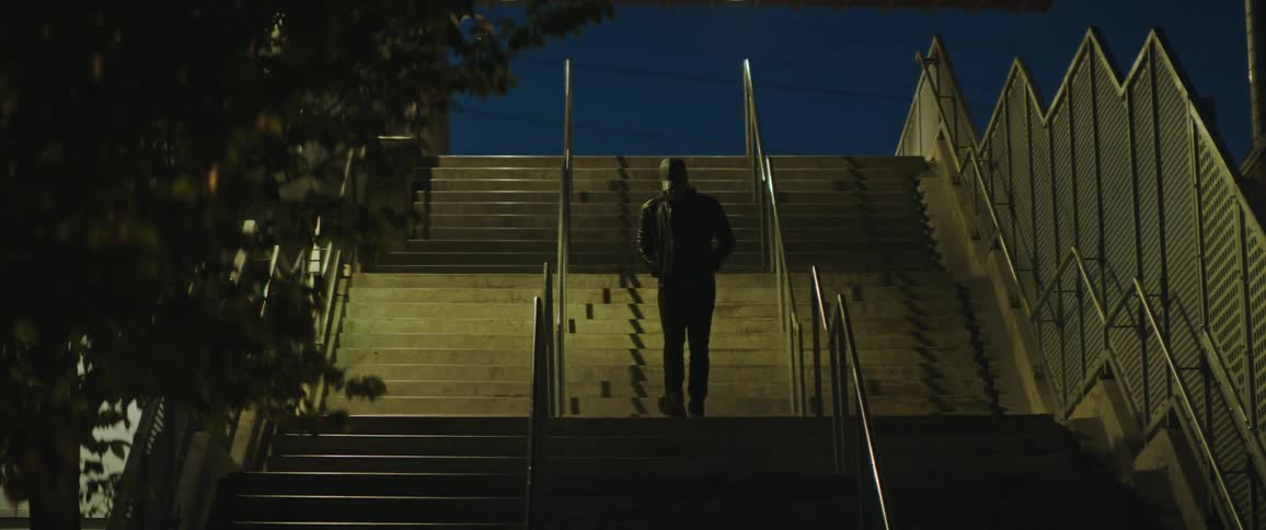 Man wearing jacket walks down long flight of outdoor stairs at building at night
