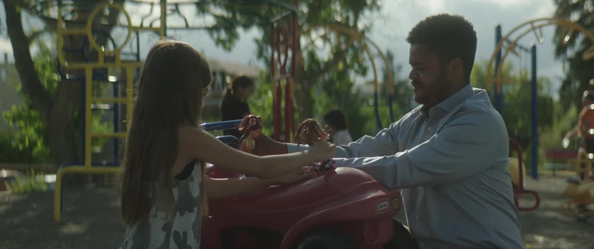 Father and his daughter play with dolls at playground as other families playin the background