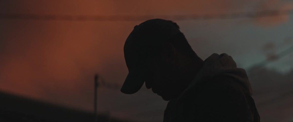 A man looks down as he stands in a dark room then he puts on his hat and leaves