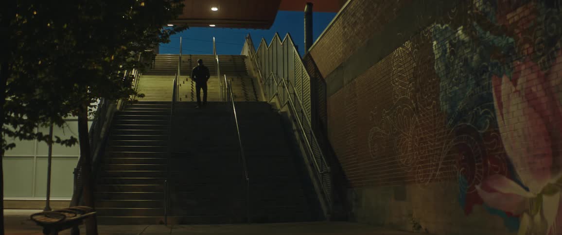 Man wearing jacket walks long outdoor stairs and past mural painted onto brick wall