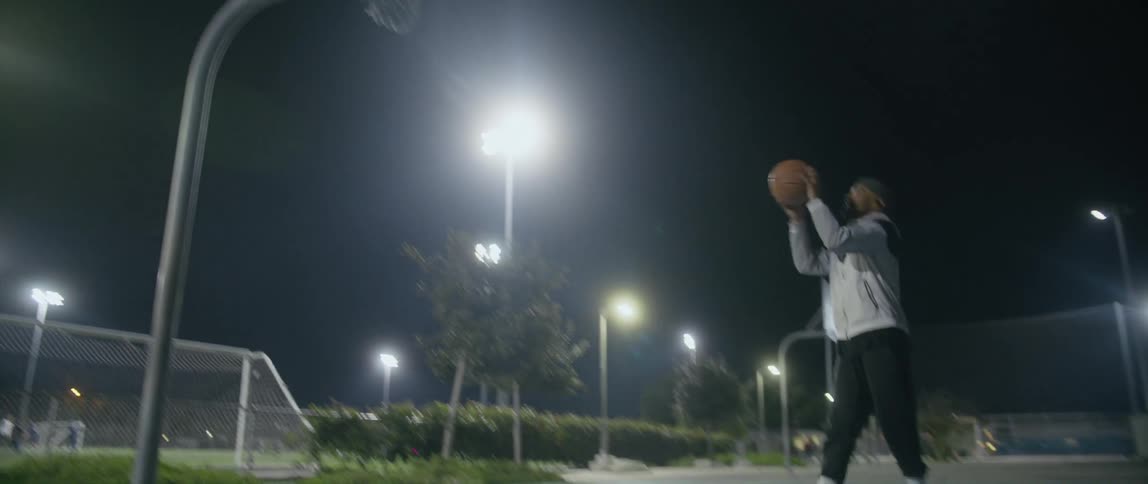 A man is in a public park after dark playing basketball alone