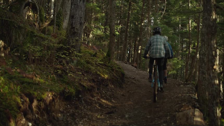 Two teenage boys bike up a hill in a forest