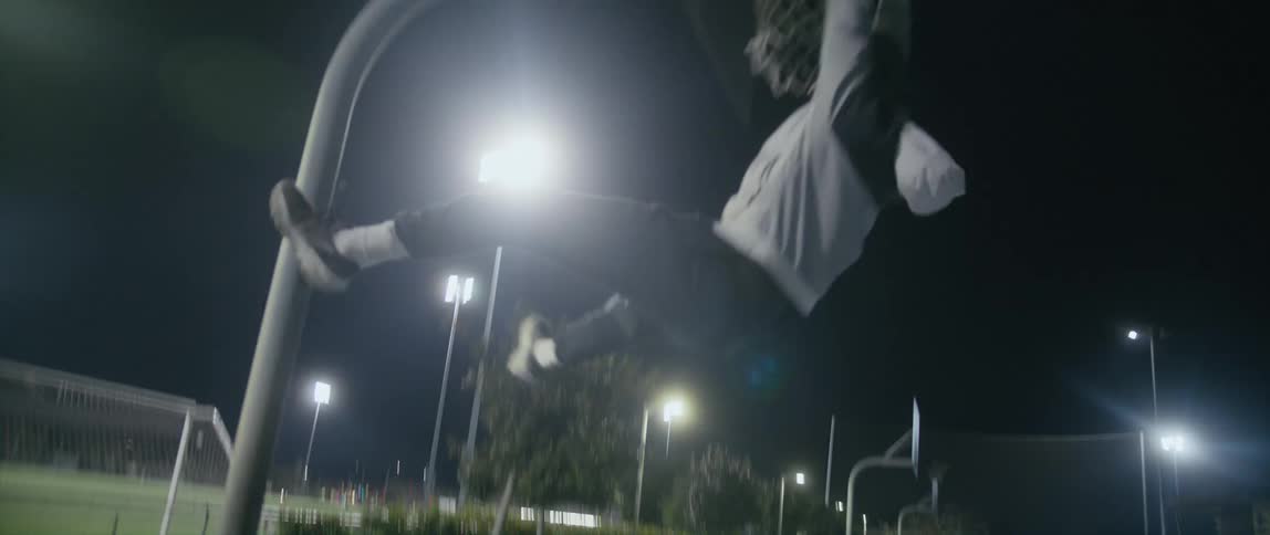 A man runs and jumps to grab onto a basketball hoop at the park