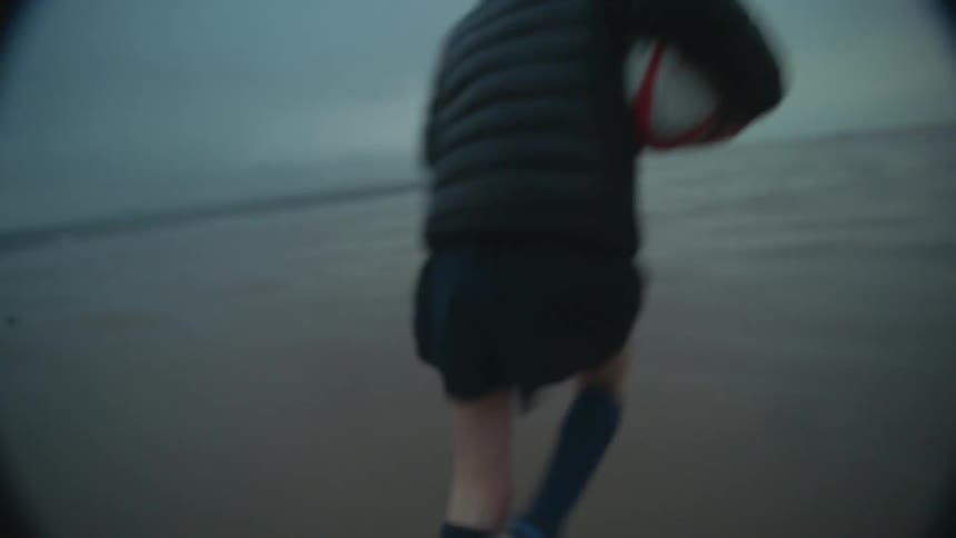 Two boys are running on a beach as one boy throws a football to the other boy