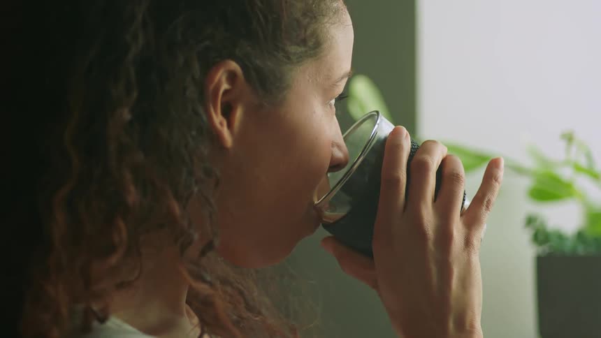 A woman is in her house and drinking out of a glass