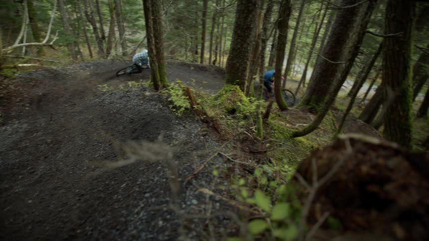 Two cyclists ride mountain bikes down sloping dirt path in forest