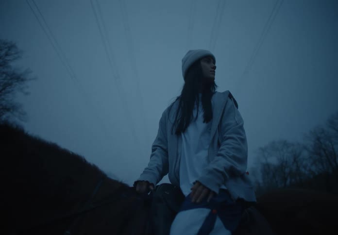 A woman on a horse near a forest looks at her surroundings
