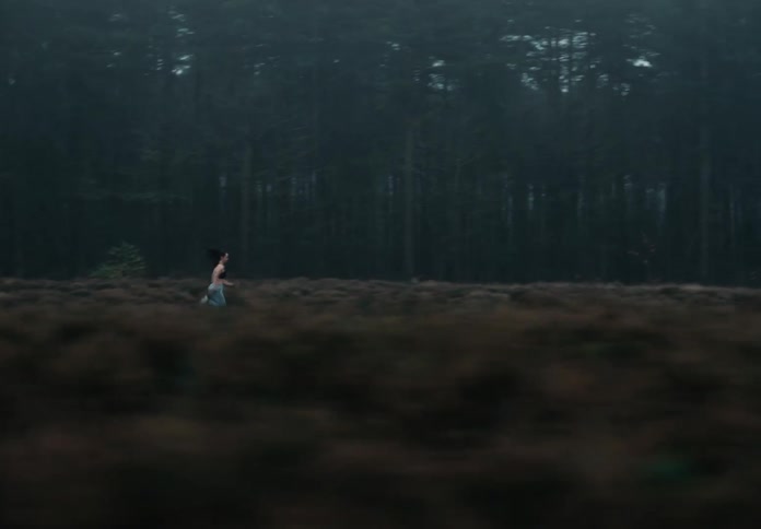A female athlete sprints through a field alongside a forest