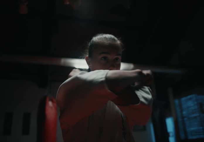 A young woman a karate outfit leans her head back and crosses her arms and bows forwards