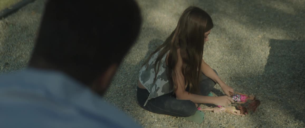 Father with blue shirt looks at daughter playing with dolls on the sand