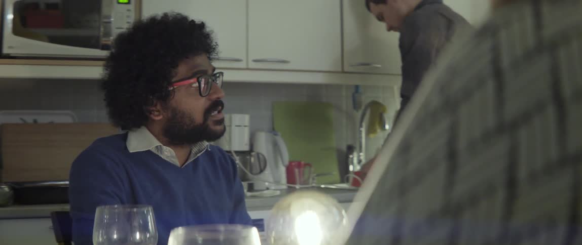 A man sits at a table in a kitchen talking to someone off camera