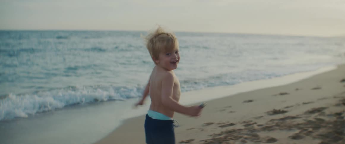 A little boy running on the beach looks back laughing as if being chased