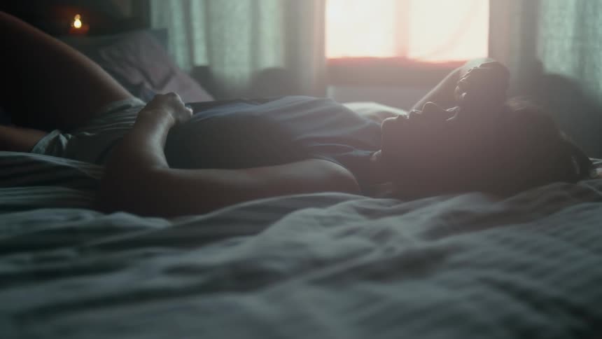 A woman lays on a bed in silence during the daytime