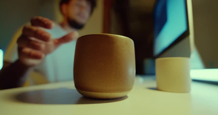 A man takes a drink from a small cup while sitting at a computer desk