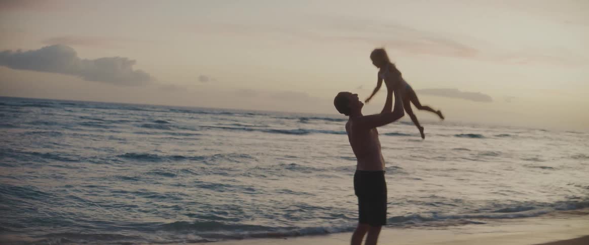 Dad makes his daughter laugh throwing her up in the air and twirling around on the beach