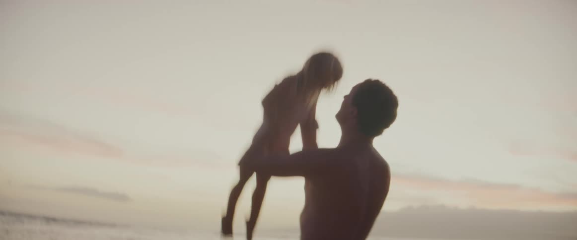 A man is playing with his young daughter on the beach swinging her around and tossing her into the air