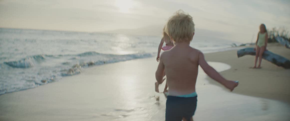A young boy runs along a beach towards a pair of girls
