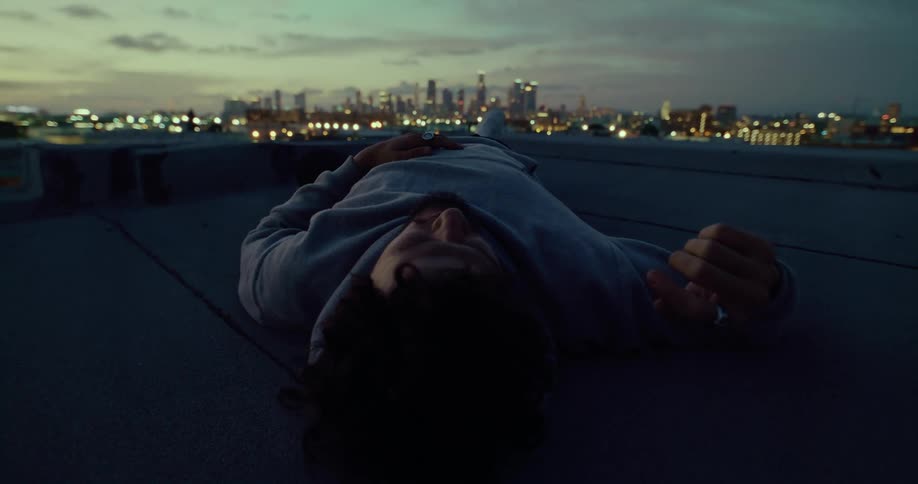 A man rests on his back on a rooftop in a metropolis at sunset