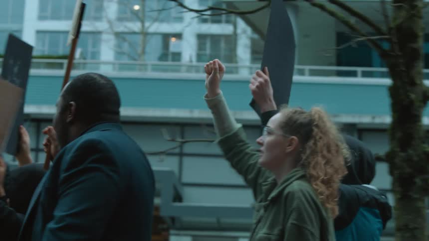 People march down a city street waving their fists and signs in the air during a rally