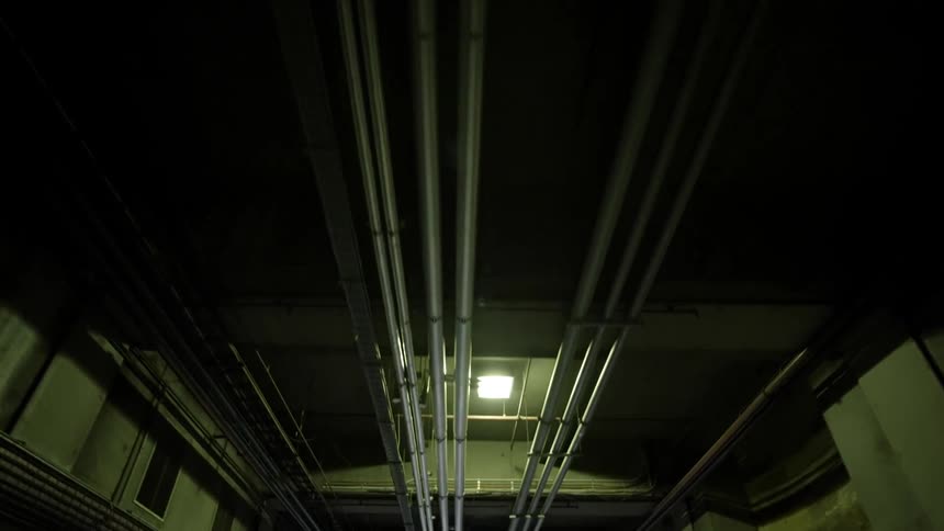 Several pipes run along the ceiling of a long corridor
