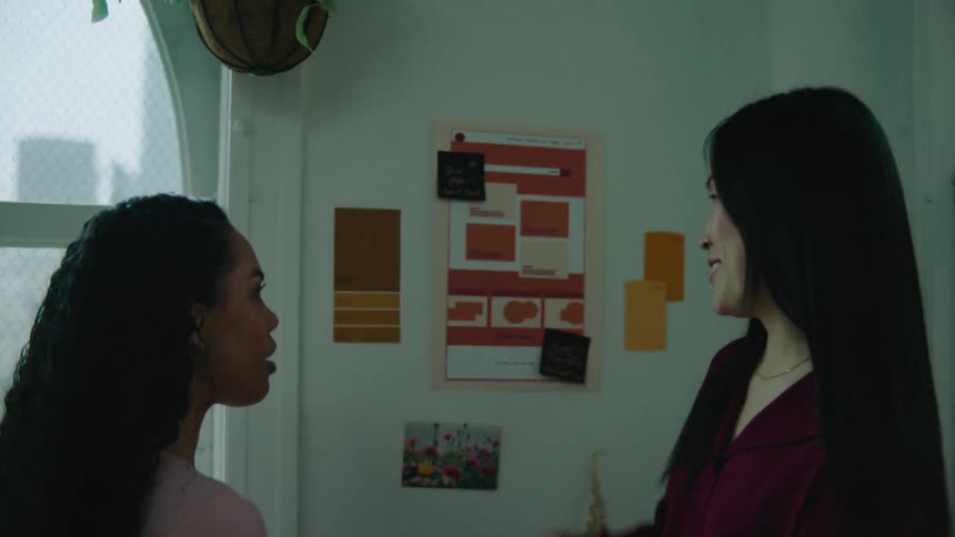 Two women stand in an office and talk as they look at paint samples on a wall