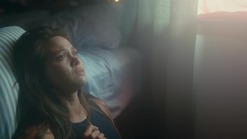 A woman cries while sitting on the floor against her bed