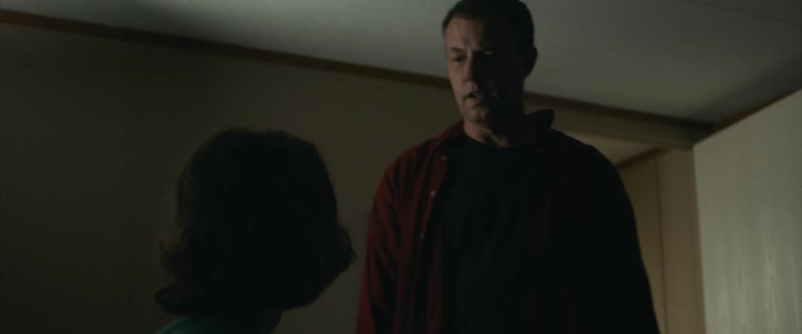 An angry looking man walks in to a bedroom and looks at a boy sitting on a bed