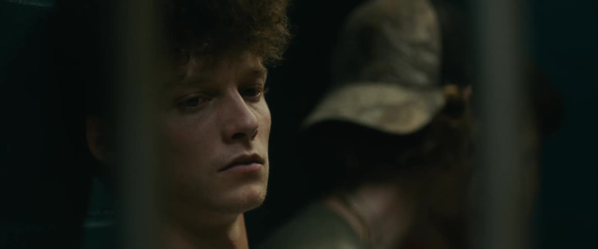 A young man sitting behind bars looking despondent as the person next to him talks