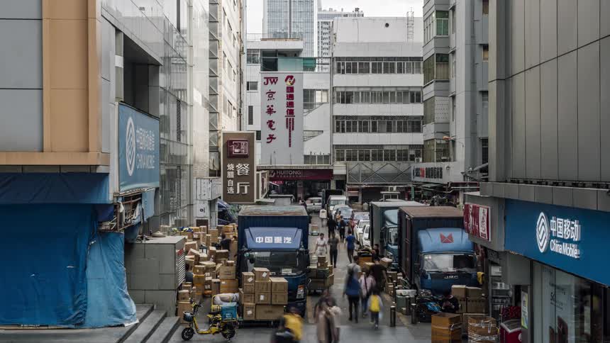 A time lapse of people walking on a street past stores as shipping boxes are loaded on to trucks