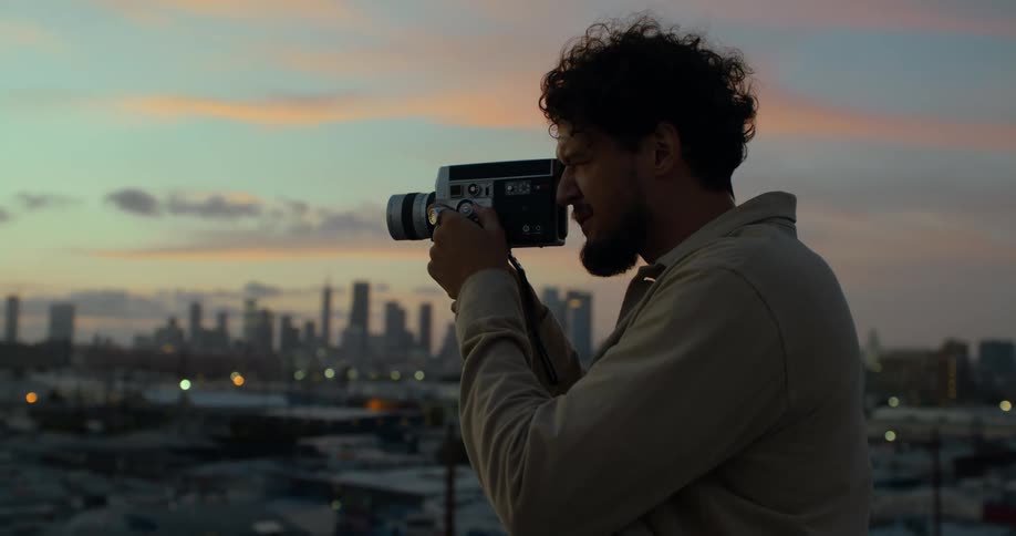 A man uses a vintage video camera to record footage of a city from a high vantage point