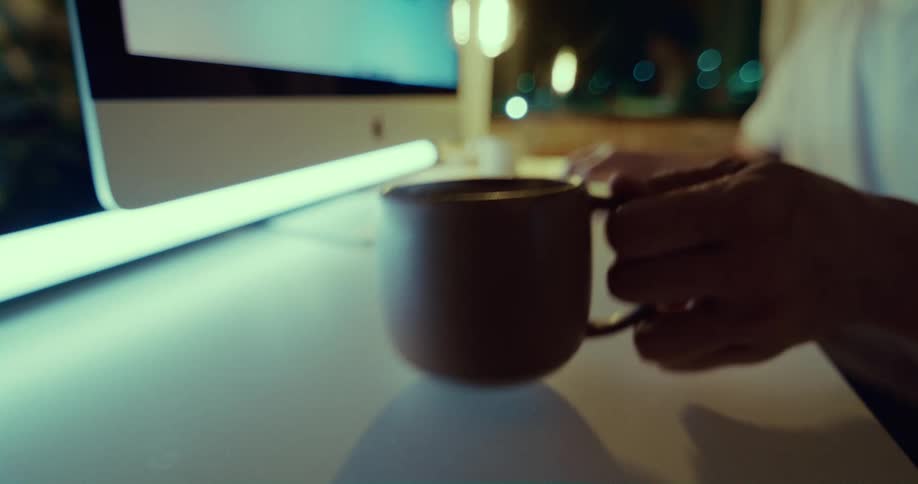 A person drinks from a mug by the computer