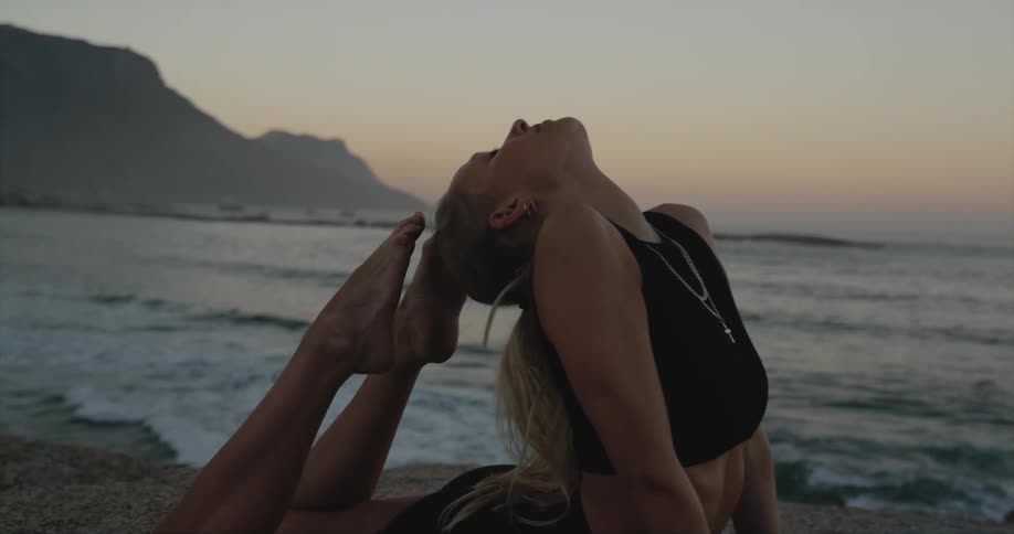 A woman on the beach touches her toes to her head as she exercises