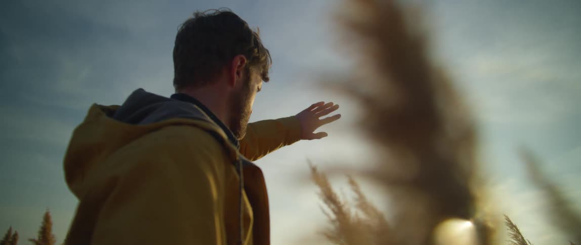 A man raises his hand to shield his eyes from the sun while standing in a field
