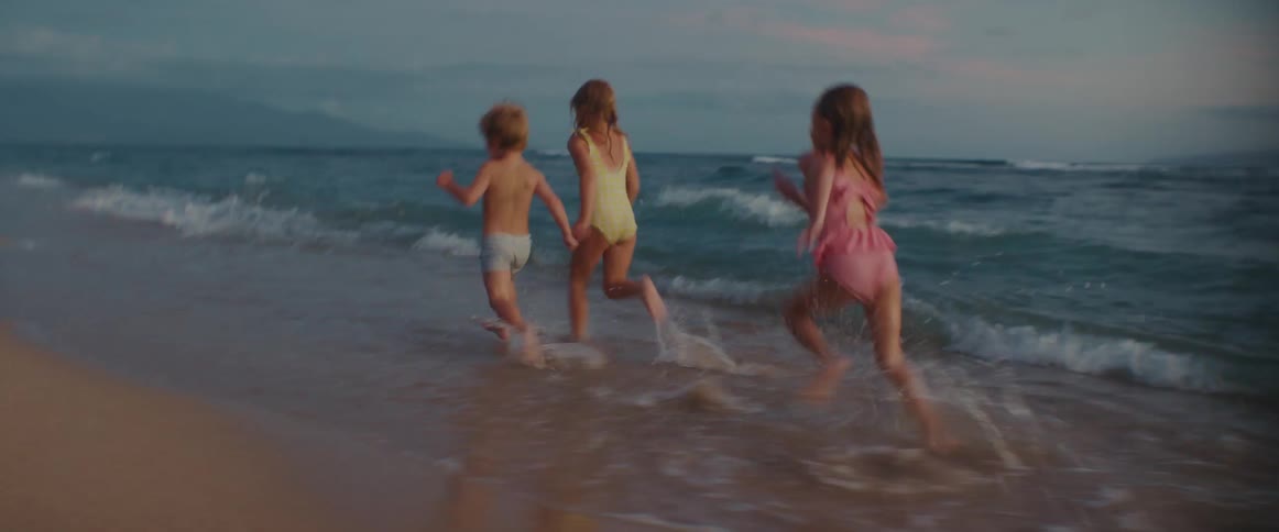 Three young children run through ocean beach waves on a quiet beach