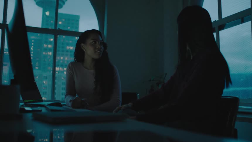 Businesswomen sitting at a desk use a computer in the office at dusk