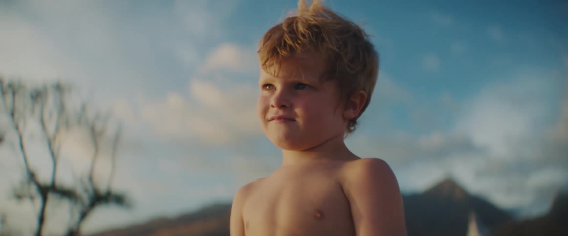Boy smiles briefly then stands staring with sister and mountains in the background