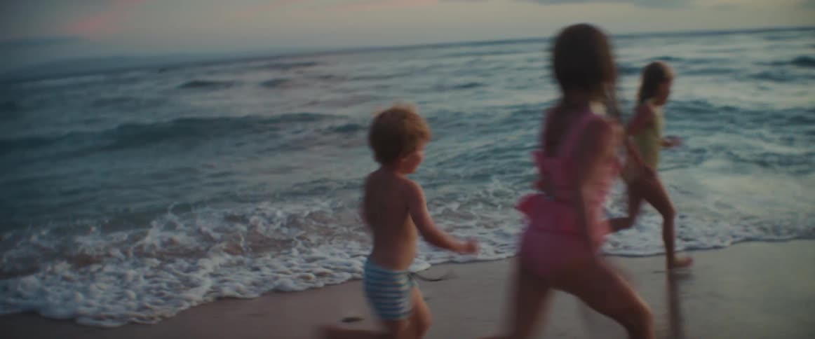 A boy runs after his sisters on the beach