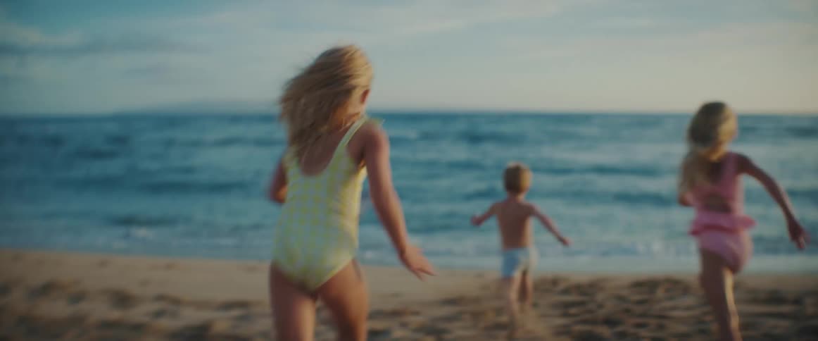 Three young children are running into the water at a beach