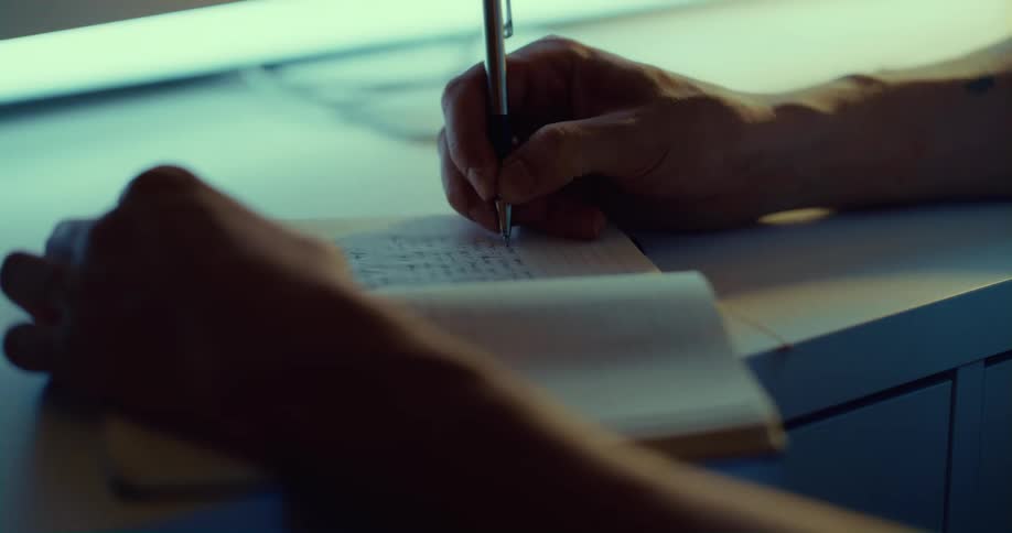 A persons hand using a pen to write on a small notebook
