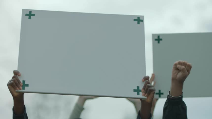 Protestors hold up signs and their hands in a fist